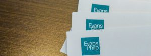 Close up of white Evans Philp letterheads spread out on a brown wooden table.